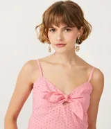 Blusa musculosa de color rosado confeccionada en tejido laise de algodón. Presenta un escote en V con un lazo decorativo en el frente, tirantes finos y detalle de lastex en la espalda para un mejor ajuste.