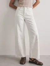 Jean blanco de tiro alto y corte wide leg, con diseño de bordados sutiles en tono sobre tono.