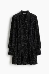 Vestido corto negro con estampado de lunares blancos, escote en V con volados, mangas largas abullonadas y cordón ajustable en la cintura.