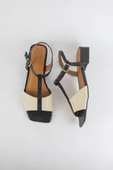 Sandalias de cuero combinadas en negro y marfil, con diseño de tiras en T, taco cuadrado bajo y pulsera con hebilla ajustable al tobillo.