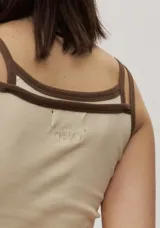 Musculosa de tejido rib color beige con detalles en marrón oscuro en el escote y doble tirante fino. Presenta un pequeño texto estampado en el pecho.