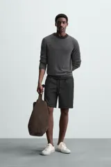 Bermuda negra de corte recto, con cintura elástica ajustable mediante cordón, pliegues frontales y bolsillos de vivo en la espalda. El bajo tiene un dobladillo vuelto.