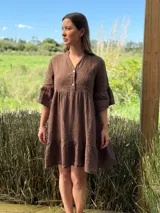Vestido corto de lino color marrón, con cuello mao, escote con botones, mangas tres cuartos con volados y ruedo con volado.