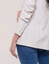 Blazer de silueta semientallada color beige, confeccionado en sastrería liviana de corte fluido, con solapa de muesca clásica, cierre frontal de un solo botón, bolsillos frontales con solapa y mangas largas.