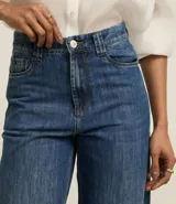 Pantalón de jean de corte wide leg, tiro alto, con bolsillos delanteros y traseros, trabillas para cinturón y cierre frontal con cremallera y botón.
