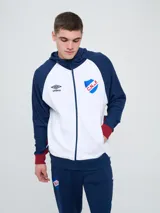 Campera deportiva Umbro del Club Nacional de Football, modelo con capucha, cierre frontal, bolsillos laterales y mangas raglán. Diseño en color blanco con mangas y detalles en azul marino y rojo.