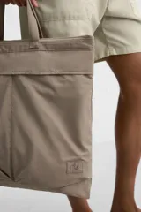 Bolso tipo shopper de tejido técnico color beige, con dos asas de mano y una correa de hombro ajustable y extraíble. Presenta un compartimento principal con cierre de cremallera, un bolsillo interior con cremallera y dos bolsillos frontales con cierre de botón a presión.