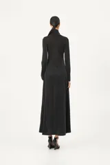 Vestido largo negro de manga larga y cuello tortuga, con silueta ajustada en el torso y falda amplia con aberturas laterales. El tejido presenta un brillo sutil.