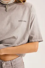 Remera gris de corte relajado, con cuello redondo, mangas cortas y pequeño estampado en el pecho.