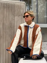 Campera de corderito con diseño de bloques de color, confeccionada en tejido sintético de textura suave. Presenta cierre frontal, cuello alto y ribetes en contraste en los bordes.
