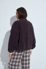Campera de corderito color marrón oscuro, con cuello camisero y cartera frontal en tela lisa a tono. Presenta cierre mediante botones a presión y mangas largas con puños elásticos.