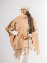 Ruana de tejido suave en color beige, con diseño envolvente y terminaciones con flecos en el ruedo.