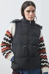Chaleco puffer negro con diseño acolchado, capucha desmontable y cierre frontal. Cuenta con cordones ajustables en la cintura y bolsillos laterales.