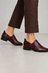 Botín plano de cuero color borravino con diseño combinado, con parte delantera lisa y talón con textura efecto reptil. Cuenta con calce tipo slip-on y suela baja.