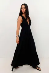 Vestido largo negro con brillo sutil, escote profundo en V y cintura marcada con frunces. Diseño sin mangas y falda amplia.