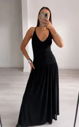 Vestido largo negro con escote profundo en V, tirantes finos y diseño ajustado en la cintura con detalle fruncido, que se abre en una falda fluida y amplia.