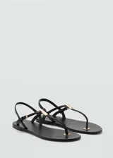 Sandalias planas de cuero caprino color negro, con diseño de tiras finas, detalle metálico en la T y cierre de hebilla en el talón.