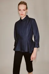 Camisa de denim azul oscuro con cuello solapa, manga larga con puños y diseño peplum en el bajo. Presenta cierre frontal con botones ocultos por solapa.