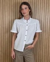 Camisa Magui blanca de manga corta, con cuello alto con volados, botonadura frontal con botones carey y detalles fruncidos en el canesú.