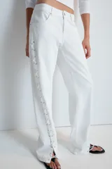 Jeans rectos de tiro medio en color blanco, con cinco bolsillos, trabillas y cierre frontal con cremallera. Presenta detalle de cordones cruzados con ojalillos metálicos a lo largo de los laterales de ambas piernas.
