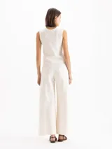 Pantalón de denim de algodón pima color blanco off-white, de tiro alto y silueta amplia de corte ancho. Presenta costuras verticales visibles y broches metálicos decorativos y funcionales en los laterales.