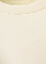 Camiseta color crudo de manga corta y cuello redondo, con diseño cruzado que forma un lazo lateral para anudar.