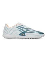 Championes de fútbol Under Armour U Shadow Slct 4 Turf, color blanco con diseño gráfico abstracto en azul y verde oscuro, con detalles en naranja claro. Suela de goma con tapones multidireccionales para césped artificial.