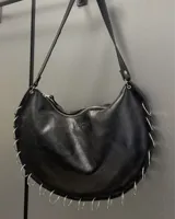 Cartera de hombro tipo hobo en color negro, confeccionada en cuero con acabado suave. Presenta un diseño de media luna con cierre superior y detalle de múltiples argollas metálicas plateadas dispuestas a lo largo del borde inferior y lateral. Incluye correa fija y el logo de la marca grabado discretamente en el frente.