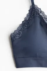 Soutien azul marino confeccionado en punto suave sin costuras, con copas triangulares con relleno extraíble y ribete de encaje en el escote. Presenta doble tirante ajustable en cada hombro y banda elástica inferior.