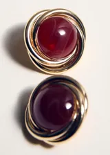Aros circulares con diseño entrelazado dorado y una piedra central de resina color burdeos.