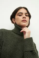 Polera de cuello alto con textura tramada, manga larga con puños acanalados y diseño holgado.