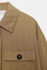 Chaqueta corta de color verde militar, con cuello solapa, bolsillos delanteros con solapa y cierre frontal de botones ocultos. Presenta mangas amplias con vuelta en los puños que muestran un forro a rayas.