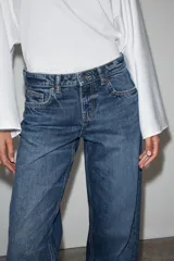 Jeans de mezclilla en color negro gastado, tiro bajo, corte de pernera recta y diseño clásico de cinco bolsillos con cierre frontal de cremallera y botón metálico.