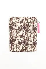 Porta laptop con estampado de animal print estilo vaca en tonos marrón y crudo, cierre superior y tirador de tela rosa.