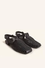 Sandalias planas tipo huarache de cuero negro, con tiras entrelazadas a mano y tira ajustable en el talón con hebilla metálica.