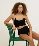 Soutien tipo top de color negro, confeccionado en tejido seamless texturizado con tirantes finos ajustables. Cuenta con copas desmontables y diseño sin costuras.