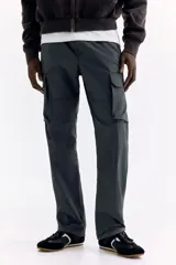 Pantalón cargo gris oscuro de nylon con corte estándar, cintura elástica con cordón ajustable, bolsillos con cierre en los laterales y bolsillos de parche con solapa en las piernas.