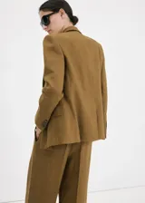 Blazer de lino color verde militar, de corte recto y diseño estructurado, con cuello en pico y solapas de muesca. Presenta mangas largas con puños abotonados, bolsillos con solapa en la parte delantera y cierre frontal de botonadura doble con abertura posterior en el bajo.