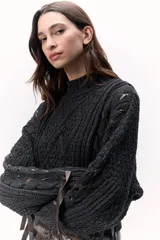 Sweater de lana merino tejido en punto grueso, color gris oscuro, con cuello alto. Presenta un diseño calado con tientos de cuero marrón insertados a lo largo de la prenda, simulando un lazo o detalle orgánico.