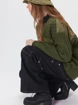 Campera tejido grueso y abrigado color verde militar, con forro de nylon interno, cuello estilo camisa en color negro y cierre frontal con botones. Cuenta con cuatro bolsillos delanteros con apliques en distintos tonos y texturas, y un parche bordado circular en el bolsillo superior izquierdo.
