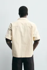 Camisa de corte relajado confeccionada en tejido de algodón, con cuello bowling y manga corta. Presenta un diseño con bordados geométricos a tono y cierre frontal de botones.
