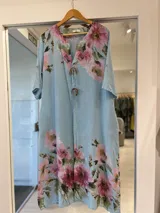 Vestido midi celeste de lino con estampado floral en tonos rosados y verdes, escote en V con cordones y apliques de argollas de madera, y mangas cortas con presilla.