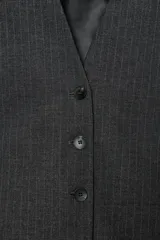 Chaleco de sastre con escote en V, cierre frontal con botones y diseño de hombros caídos. Presenta un estampado de raya diplomática sobre fondo gris oscuro.