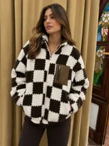 Campera de corderito sintético con diseño de cuadros damero en color crudo y chocolate. Presenta cierre frontal completo, cuello alto y un bolsillo frontal tipo cargo en material sintético con cierre.