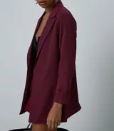 Blazer de sastrería color bordó, de corte oversized y largo, confeccionado en crepé. Presenta solapas clásicas, bolsillos frontales y detalle de pliegues en los puños.