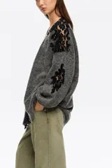 Cardigan largo de punto oversize en color gris, con escote en pico y cierre frontal de botones. Presenta mangas largas con volumen y detalles de encaje negro a contraste en hombros y mangas.