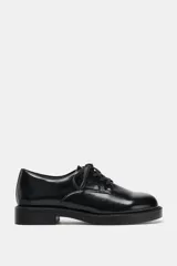 Zapato tipo blucher de estilo clásico con cierre mediante cordones. Presenta un acabado en punta redonda y suela con plataforma.