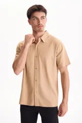 Camisa de manga corta de lino color beige, con cuello camisero y cierre frontal de botones.