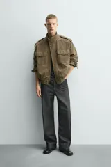 Cazadora de corte relajado confeccionada en piel con acabado de ante. Presenta cuello subido, cierre frontal de cremallera oculta por solapa con botones a presión, bolsillos de plastrón con solapa en el pecho y bolsillos de vivo en la cadera. Incluye trabillas en los hombros, mangas largas con puños abotonados y bajo con elástico.