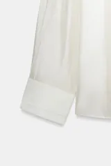 Camisa de mujer fluida de ZARA WOMAN COLLECTION, confeccionada en hilatura con mezcla de lyocell. Presenta escote en pico, manga larga con puños marcados y bajo asimétrico, con cierre frontal de botones ocultos.